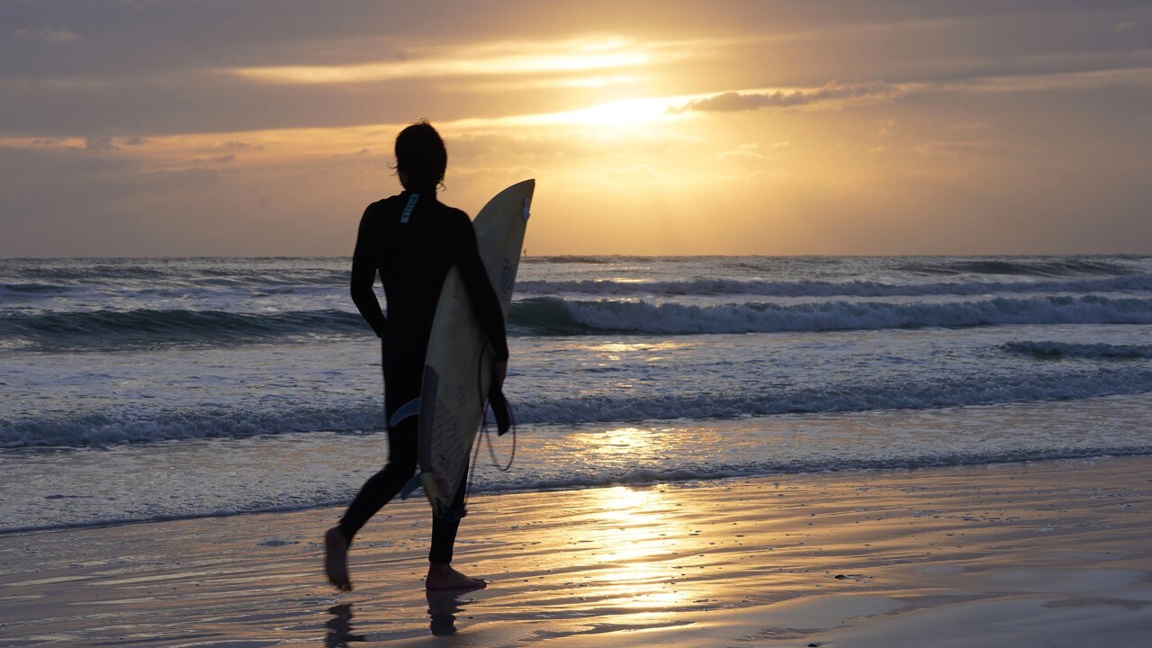 A surfer strolls along Siesta Key Beach at sunset