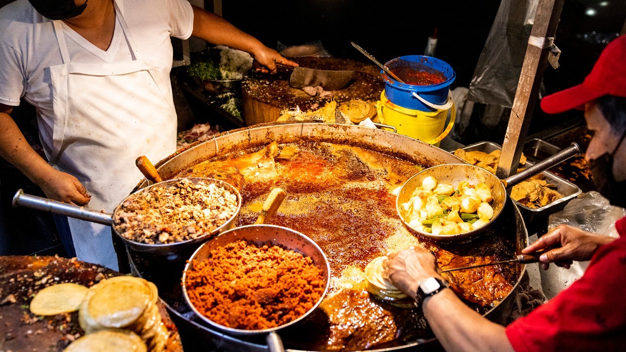 Cooks fry meat and tortillas for hungry people at a taco stand in Mexico City.