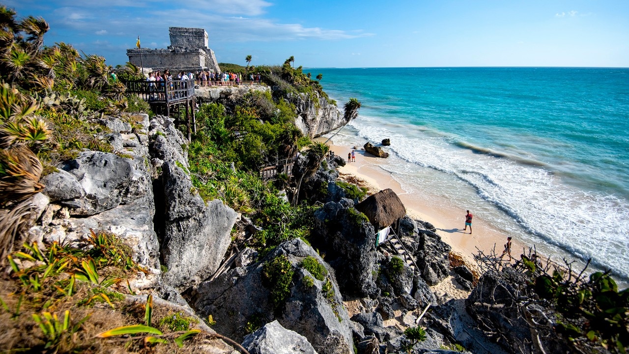 Visitors to the Mayan city of Tulum stroll along Playa Ruinas below the site's main pyramid, El Castillo.